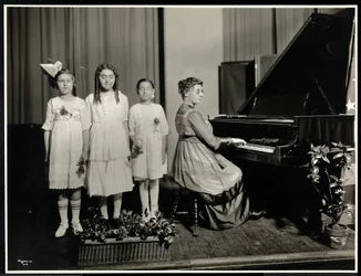 Mujer tocando el piano mientras tres niñas cantan en la Asociación para Ciegos de Nueva York, 111 East 59th Street, Nueva York, c.1917